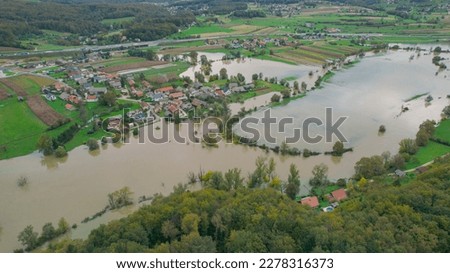 AERIAL: Raised river water approaches village after spilling over riverbanks. Large areas of rural land area are under floodwater of the swollen river. Flooded countryside after heavy rains in fall.