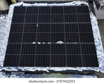 AERIAL: Rectangular array of black solar panels from above, bordered by fresh snow. Dark surface contrasts with white surroundings. Domestic use of sustainable technology for electricity production.