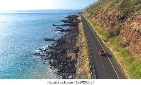 AERIAL: Red convertible car driving along the picturesque coastal road above the great ocean cliffs and sea water splashing into rocks. Happy young couple on summer vacation traveling at the seaside - Powered by Shutterstock