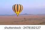 AERIAL: Safari hot air balloon flying above vast savanna plain rolling into the distance in Serengeti National Park at purple light dawn. Tourists traveling in air over African wilderness at sunrise