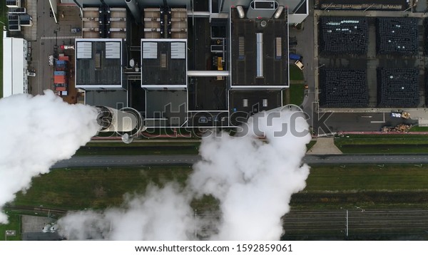 Aerial satellite view\
of coal fired power station is a thermal plant which burns a fossil\
fuel to produce electricity by converting heat of combustion into\
mechanical energy
