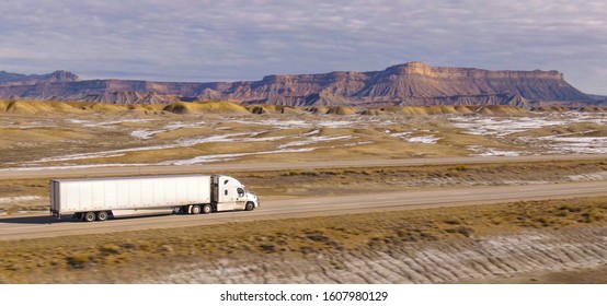 AERIAL: Semi-trailer truck speeds along the motorway running across the desert in Utah. Wintry desert landscape surrounds truck driving down the interstate highway running across rugged US wilderness.