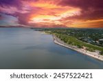 aerial shot along the coast of Lake Pontchartrain with homes, lush green trees, plants and grass, rippling water, powerful clouds at sunset in New Orleans Louisiana USA