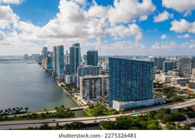 Aerial shot from balcony of suburb in Edgewater, view of Biscayne Bay, with large tropical vegetation around, modern houses and towers, commercial areas, summer weather, blue sky
