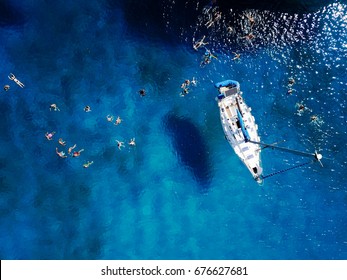 Aerial shot of beautiful blue lagoon at hot summer day with sailing boat. Top view of people are swimming around the boat. - Powered by Shutterstock