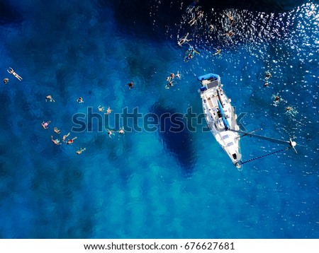 Aerial shot of beautiful blue lagoon at hot summer day with sailing boat. Top view of people are swimming around the boat.