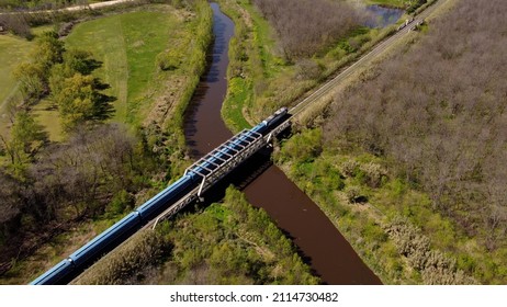 Aerial Shot Of Blue Train Passing Bridge In Rural Area Of Buenos Aires During Summer. Top Down View