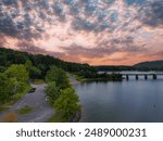 aerial shot of a bridge over the rippling waters of Lake Allatoona surrounded by lush green trees, grass and plants with powerful clouds at sunset at Red Top Mountain State park in Acworth Georgia USA