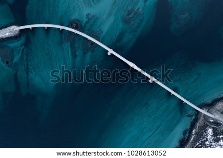 Aerial shot of a bridge over sea strait. Visible depth with blue and green colours near Tromso. Sommaroy, Norway