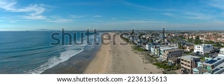 aerial shot of the coastline with blue ocean water and homes along the sand on the beach, cars driving on the street and blue sky with clouds in Huntington Beach California USA
