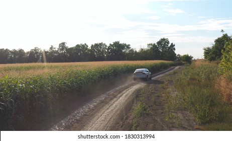 Aerial Shot Of Electric Car Riding Through Empty Rural Road. Camera Following To Modern Vehicle Going On Ground Way Near Field. Flying Over Car Driving Through Countryside Path At Sunny Day. Slow Mo.