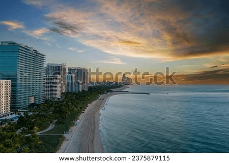 aerial shot of hotels, luxury condos and skyscrapers along the coastline at sunrise at Bal Harbour Beach, blue ocean water, silky sand and lush green trees and grass in Miami Beach Florida USA