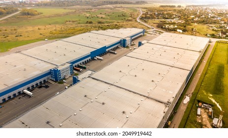 Aerial Shot Of Industrial Warehouse. Loading Hub And Many Trucks With Cargo Trailers. Aerial View Of Goods Warehouse. Modern Distribution Center From Outside. Aerial View Of Warehouse With Trucks. 