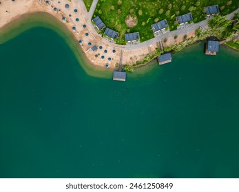 Aerial shot of a lakeside with sandy beach and cabins on a clear day, showcasing leisure and relaxation - Powered by Shutterstock