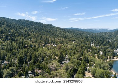 aerial shot of majestic mountain ranges covered with tall lush green trees and homes along the hillside with a lake, blue sky and clouds at Lake Gregory in Crestline California USA - Powered by Shutterstock