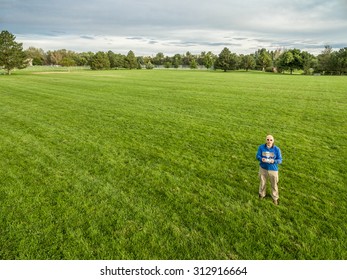 Aerial Shot Of A Male Drone Operator With A Radio Controller On A Green Grassy Field