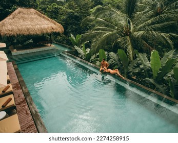 Aerial shot of man and woman relaxing at the poolside. Couple enjoying holiday at luxury resort. - Powered by Shutterstock