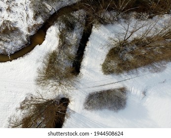 An aerial shot of a narrow river flowing through a snow-capped forest in winter