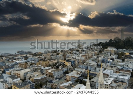 aerial shot of the ocean and streets lined with apartments, lush green trees and Coit Tower with powerful clouds at sunset in San Francisco California USA