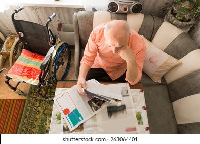 Aerial Shot of Old Man Reading Articles at Newspaper While Sitting at the Sofa with his Wheel Chair on his Side.