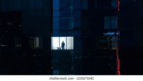 Aerial Shot: From Outside Into Office Building With Businessman Looking Out Of The Window. Beautiful Shot Of The Financial Business District Skyscrapers In The Evening.