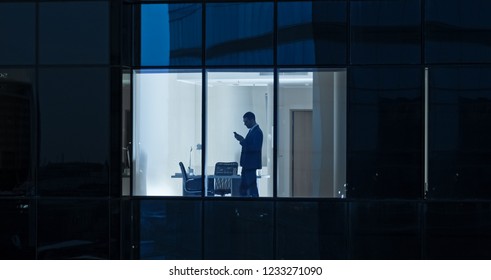 Aerial Shot: From Outside into Office Building with Businessman Using Mobile Phone and Standing by the Office Window. Beautiful Shot of The Financial Business District Skyscrapers. - Powered by Shutterstock