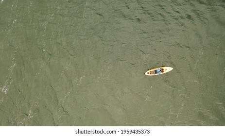 An Aerial Shot Over A Salt Marsh On A Sunny Day. In The Shot Is A Man In A Yellow Kayak On The Green Waters. The Shot Was Taken On Long Island, NY.