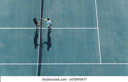 Aerial shot of professional tennis players handshakes at the net. Sportsmen shaking hands over the net on hard court. - Powered by Shutterstock