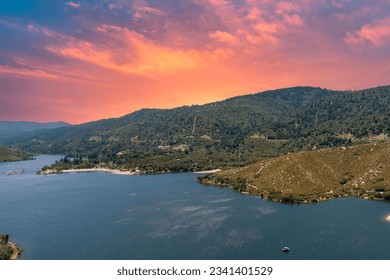 aerial shot of the rippling blue waters of Silverwood Lake with a beach, mountains covered in lush green trees, plants and grass, powerful clouds at sunset in Hesperia California USA