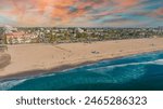 an aerial shot of the Santa Monica beach with people relaxing in the sand near the blue ocean water with color umbrellas, the cityscape with buildings and trees with powerful clouds in California	