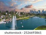 aerial shot of the skyscrapers, office buildings and hotels in the city skyline, a lake with people in pedal boats, green trees and grass, powerful clouds at sunset in Los Angeles California USA