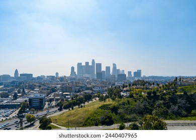 aerial shot of skyscrapers, office buildings and hotels in the city skyline with cars driving on the freeway, lush green trees and grass with blue sky in Los Angeles California USA - Powered by Shutterstock