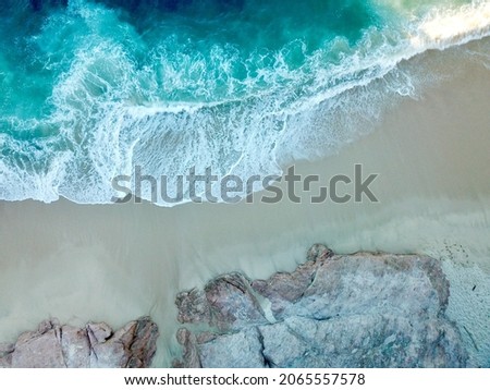 An aerial shot of a sunny beach with blue water and rocks