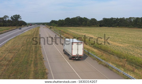 Aerial shot of truck with cargo trailer driving on\
road and transporting goods. Flying over delivery lorry moving\
along highway passing in countryside with scenic nature environment\
around. Back view.