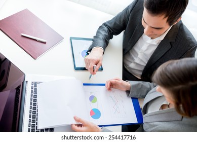 Aerial Shot Of Two Business People Reviewing Charts From Business Documents While Sitting At The Worktable.