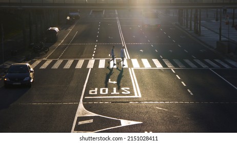 An Aerial Shot Of Two People Crossing The Road With Cars Around In Early Morning