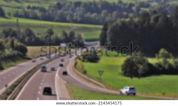 Aerial shot of a vehicle-heavy highway with\
green forest in a blurred\
background