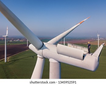 Aerial Shot Of A Worker Standing On The Top Of A Wind Turbine.