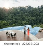 Aerial shot of young man and woman holding hands while standing by swimming pool. Couple in love near holiday resort poolside.