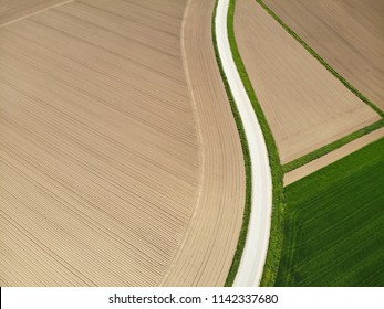 AERIAL: Spectacular empty country road winding past vast plowed fields and grasslands on a sunny summer day. Flying above a concrete route running through a scenic countryside. Breathtaking nature.