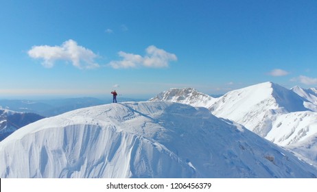 AERIAL: Spectacular sunny mountain range surrounds the unrecognizable skier taking photos of the majestic nature before skiing in the fresh powder snow covering the slopes. Beautiful winter landscape. - Powered by Shutterstock