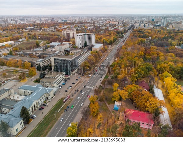 Aerial street view in autumnal\
yellow city central district. Fly above driving traffic near autumn\
city park and railroad station. Treetop view on Kharkiv,\
Ukraine