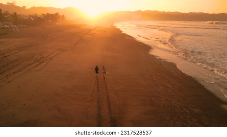 AERIAL: Stunning view of orange glowing sandy beach and rolling ocean waves. Chatty friends coming back in golden light after riding waves in Pacific. Surf couple on a surf trip at exotic Playa Venao. - Powered by Shutterstock