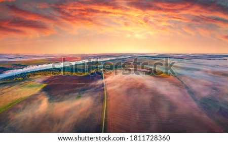 Aerial summer view from flying drone of plowed field. Amazing sunrise of Ukrainian countryside, Foggy landscape of cultivated fields with old country road, Ternopil, Ukraine, Europe. 