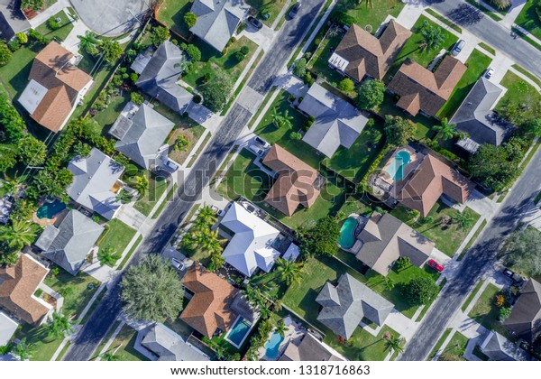 Aerial summer view of warm sunny neighborhood community\
roofs with diagonal streets and lots of houses with pools and palm\
trees. 