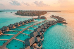 Aerial Sunset Landscape, Luxury Tropical Resort Water Villas. Beautiful Island Beach, Palm Trees, Orange Sunrise Sea Sky. Amazing Bird Eyes View Maldives Paradise  Tropical Bay. Exotic Summer Vacation