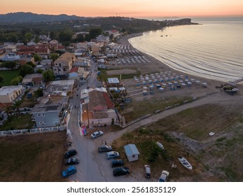 Aerial sunset view of a coastal village with beach, buildings, and parked cars. - Powered by Shutterstock