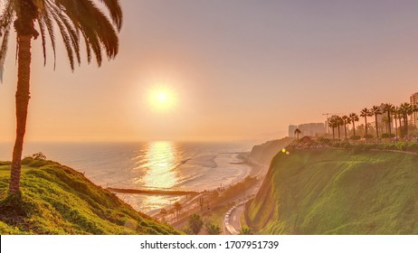 Aerial Sunset View Of Lima's Coastline In The Neighborhood Of Miraflores Timelapse With Orange Light, Lima, Peru. Road With Traffic And Beach With Ocean. Palm Near Love Park