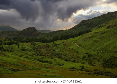 AERIAL: Threatening rain clouds hover above rolling green hills of Lake District, hinting at an upcoming downpour in a peaceful natural environment. Moody weather in a picturesque mountain region. - Powered by Shutterstock