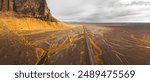 Aerial top back panoramic view vehicle drive on Icelandic southern ring road with scenic mountains and famous natural landmark - Lomagnupur mount. Iceland road trip travel concept